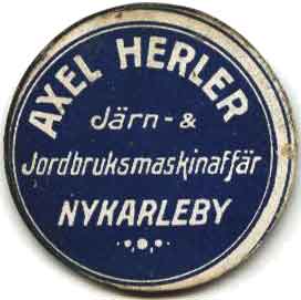 Fickspegel, diameter ca 5 cm, med reklam för Alfred Herlers Järn- & Jordbruksmaskinaffär.