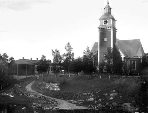 [Kyrkan från västsydväst. Gråstensplintarna från 1901 finns kring kyrkan, men inte pumphuset som byggdes för Normalskolans vattenförsörjning, så därför är det fotograferat senast 1907. Förstoring.